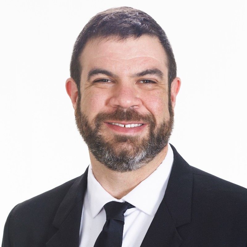 Mike Macauley, founder of Exagium, smiling in a dark suit and tie.